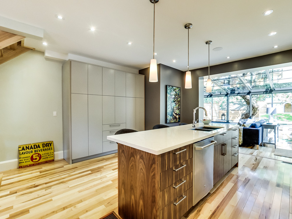 Kitchen - mid-sized transitional galley light wood floor and multicolored floor kitchen idea in Toronto with a double-bowl sink, flat-panel cabinets, beige cabinets, quartz countertops, gray backsplash, ceramic backsplash, stainless steel appliances and an island