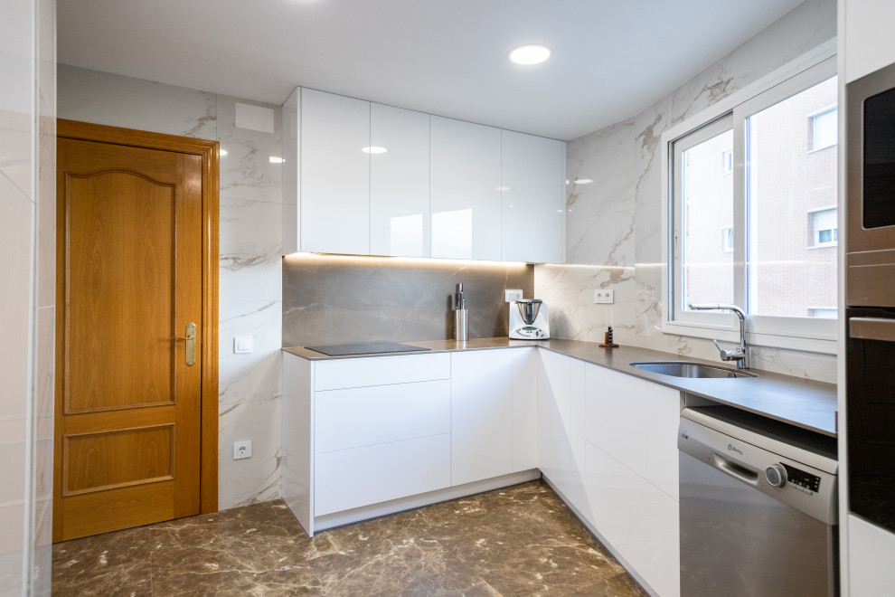 Large modern l-shaped enclosed kitchen in Barcelona with a single-bowl sink, flat-panel cabinets, white cabinets, white splashback, ceramic splashback, stainless steel appliances, terrazzo flooring, no island, brown floors and grey worktops.