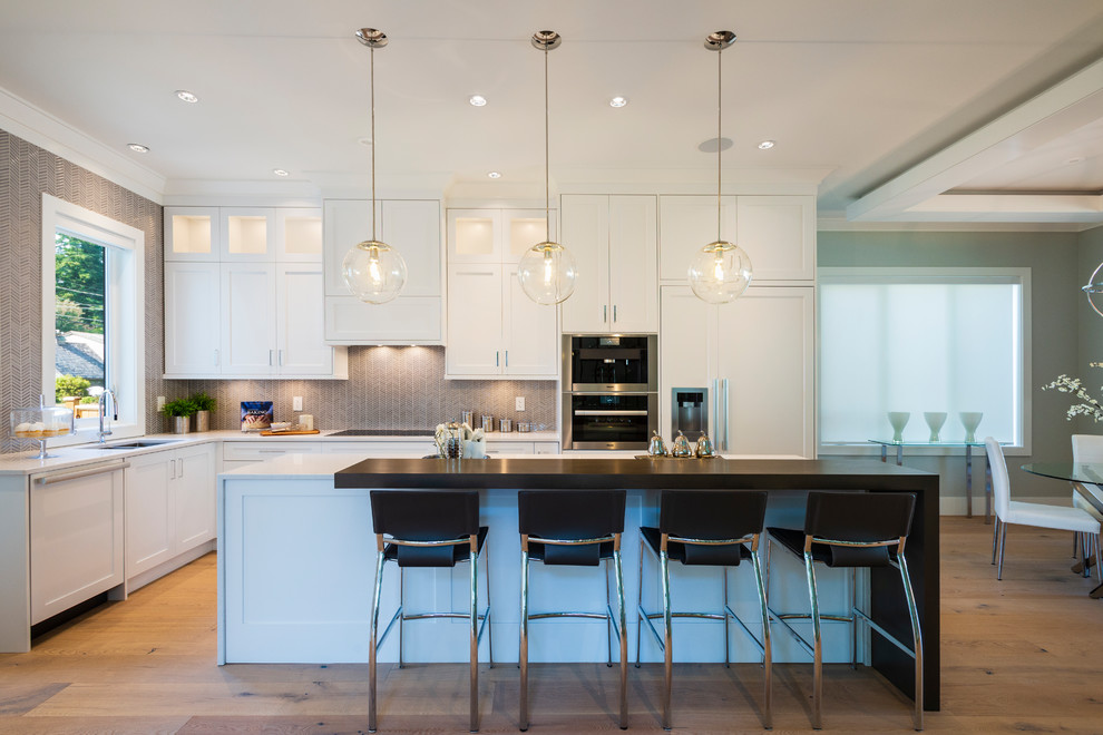 Open concept kitchen - mid-sized transitional l-shaped light wood floor and beige floor open concept kitchen idea in Vancouver with an undermount sink, shaker cabinets, white cabinets, quartz countertops, gray backsplash, mosaic tile backsplash, paneled appliances, an island and gray countertops