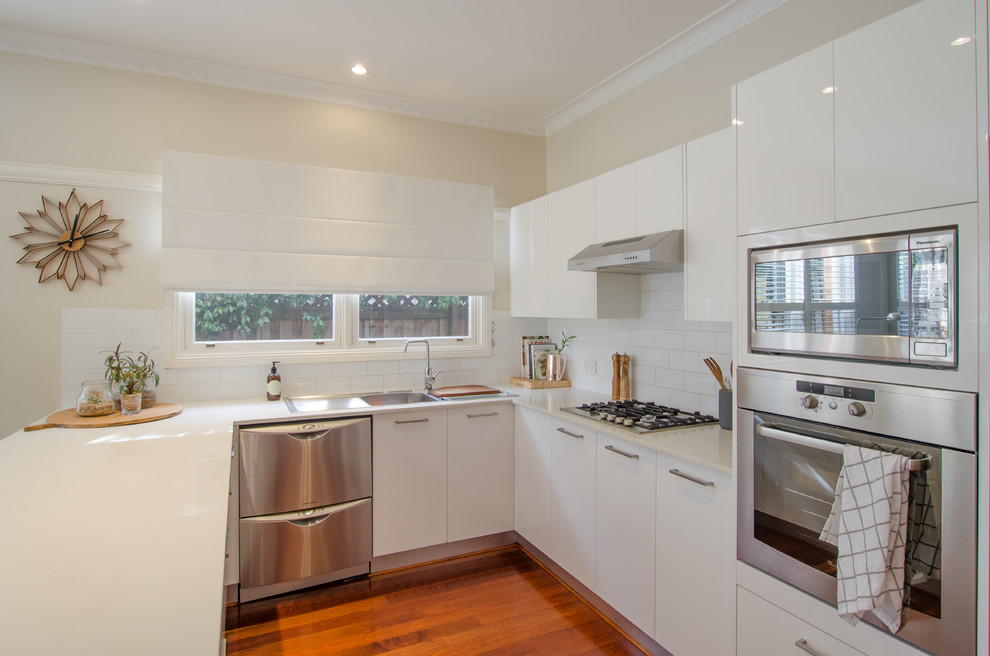 Inspiration for a mid-sized contemporary u-shaped eat-in kitchen in Sydney with a double-bowl sink, flat-panel cabinets, white cabinets, granite benchtops, white splashback, ceramic splashback, stainless steel appliances, dark hardwood floors and with island.