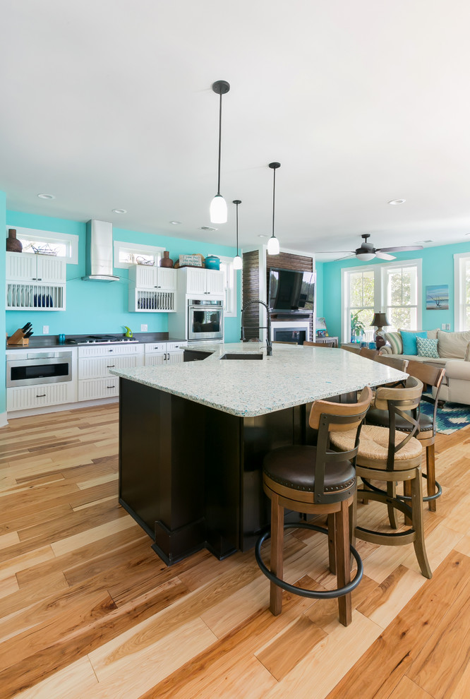 Large beach style l-shaped open plan kitchen in Charleston with a single-bowl sink, louvered cabinets, white cabinets, recycled glass benchtops, blue splashback, stainless steel appliances, medium hardwood floors, with island and brown floor.