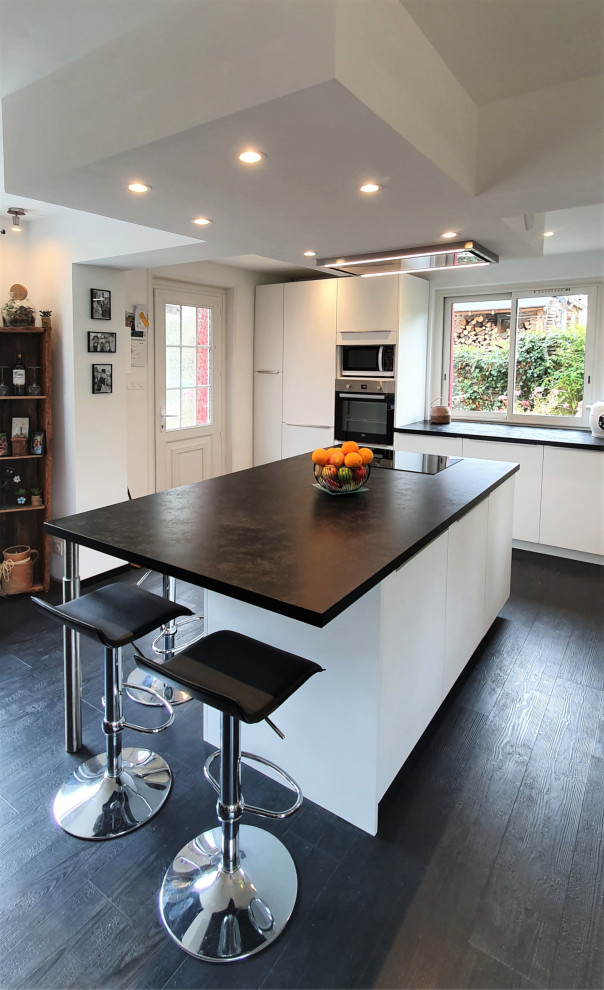 Large transitional l-shaped open plan kitchen in Other with an undermount sink, flat-panel cabinets, white cabinets, laminate benchtops, white splashback, timber splashback, panelled appliances, laminate floors, with island, black floor, black benchtop and recessed.