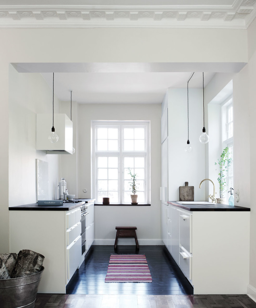 Photo of a mid-sized scandinavian kitchen in Odense with flat-panel cabinets, white cabinets, wood benchtops, white splashback, dark hardwood floors, no island and brown floor.