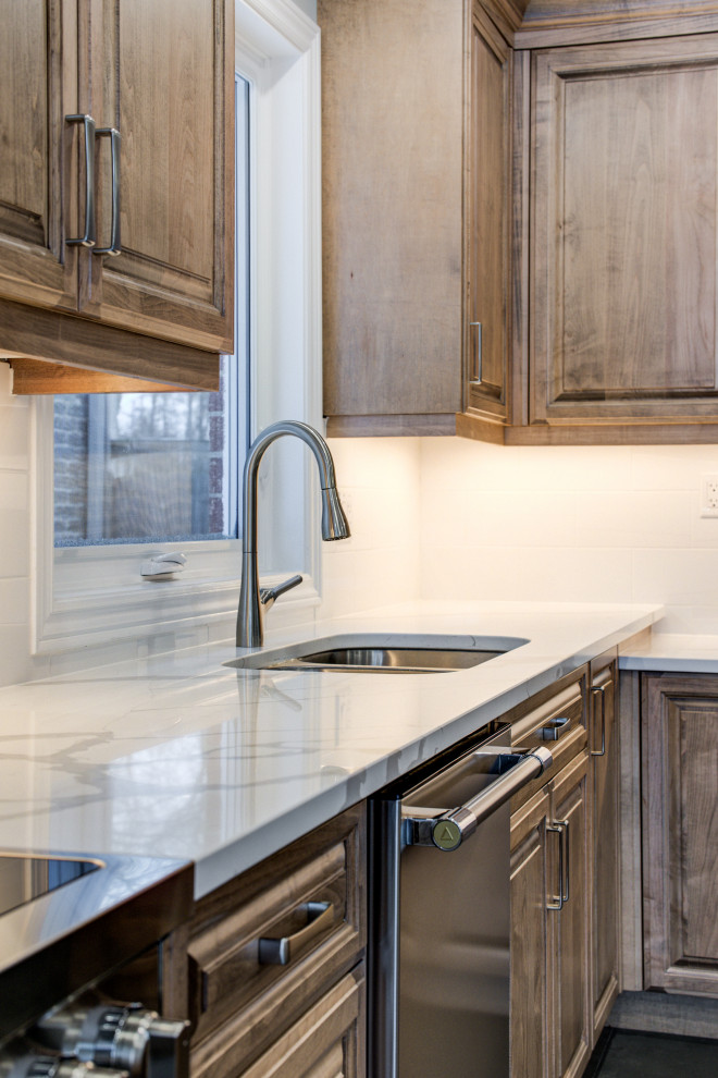 Mid-sized transitional l-shaped eat-in kitchen photo in Toronto with an undermount sink, raised-panel cabinets, medium tone wood cabinets, quartz countertops, white backsplash, ceramic backsplash, stainless steel appliances, an island and white countertops