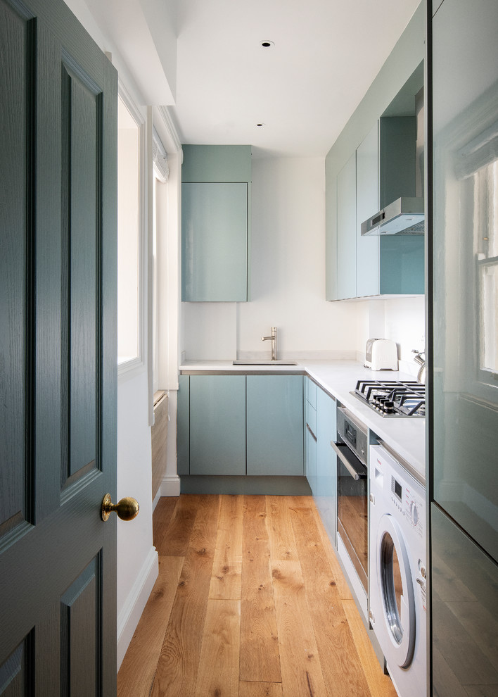 Photo of a small contemporary l-shaped separate kitchen in London with an undermount sink, flat-panel cabinets, green cabinets, white splashback, no island and white benchtop.