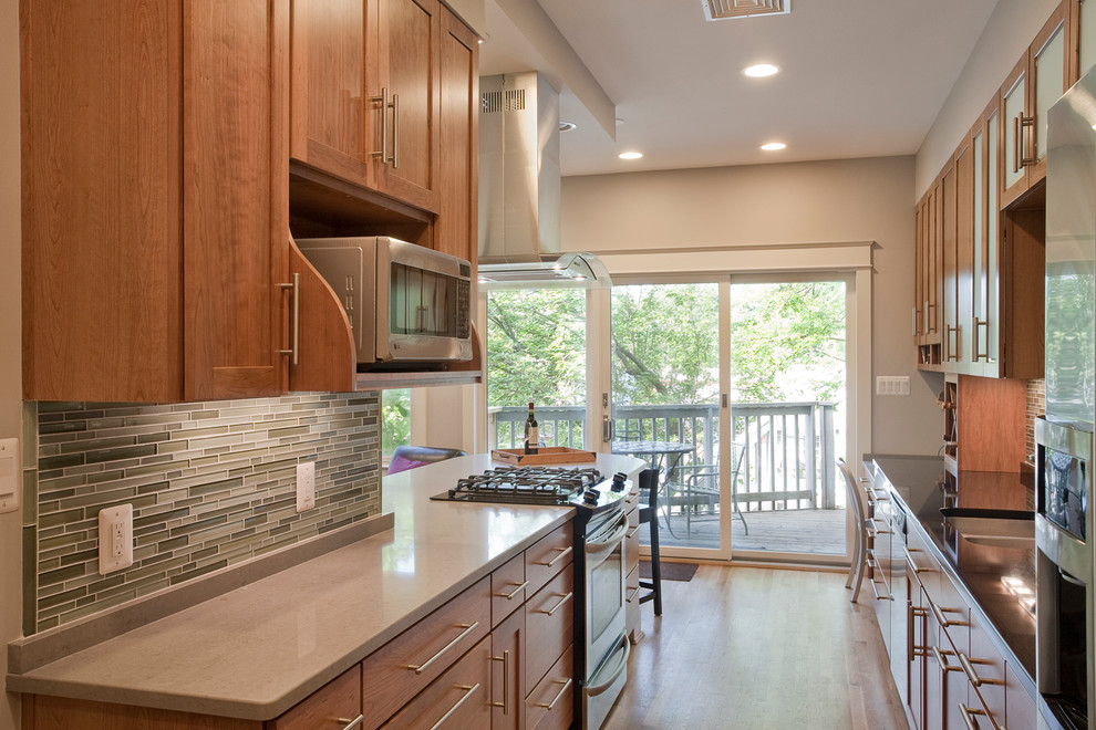 Large transitional u-shaped light wood floor eat-in kitchen photo in DC Metro with an undermount sink, glass-front cabinets, medium tone wood cabinets, gray backsplash, mosaic tile backsplash, stainless steel appliances and an island