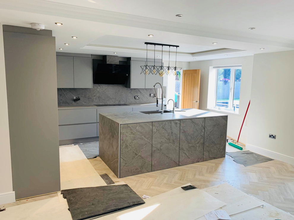 Design ideas for a mid-sized modern l-shaped open plan kitchen in Other with an integrated sink, flat-panel cabinets, grey cabinets, quartz benchtops, grey splashback, stone slab splashback, black appliances, with island, grey floor and grey benchtop.