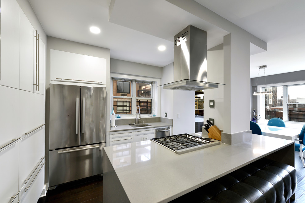 Mid-sized contemporary single-wall open plan kitchen in New York with a drop-in sink, flat-panel cabinets, white cabinets, quartz benchtops, grey splashback, porcelain splashback, stainless steel appliances, dark hardwood floors and with island.