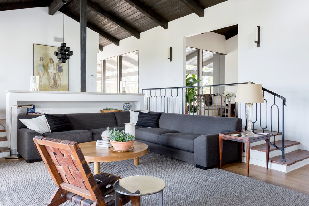 Midcentury living room in Los Angeles with white walls, medium hardwood floors and brown floor.