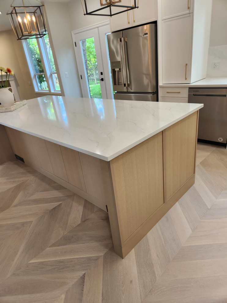 Example of a mid-sized transitional light wood floor and beige floor eat-in kitchen design in Vancouver with a farmhouse sink, recessed-panel cabinets, white cabinets, quartzite countertops, white backsplash, quartz backsplash, stainless steel appliances, an island and white countertops