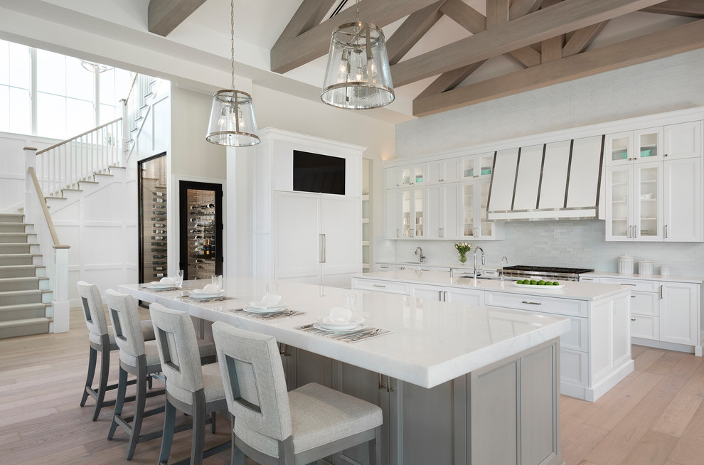 Inspiration for a large transitional l-shaped eat-in kitchen in Other with white cabinets, marble benchtops, white splashback, mosaic tile splashback, multiple islands, beige floor, an undermount sink, recessed-panel cabinets, panelled appliances, light hardwood floors and white benchtop.