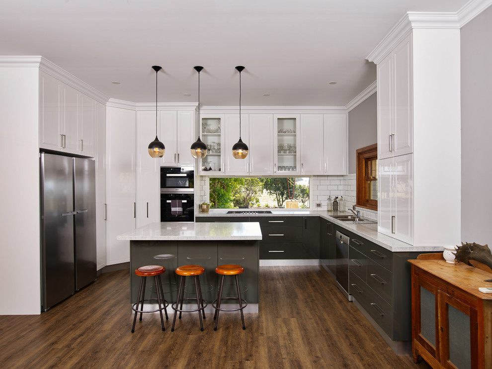 Photo of a large transitional u-shaped eat-in kitchen in Other with a drop-in sink, raised-panel cabinets, white cabinets, quartz benchtops, white splashback, subway tile splashback, with island, brown floor, white benchtop, stainless steel appliances and dark hardwood floors.