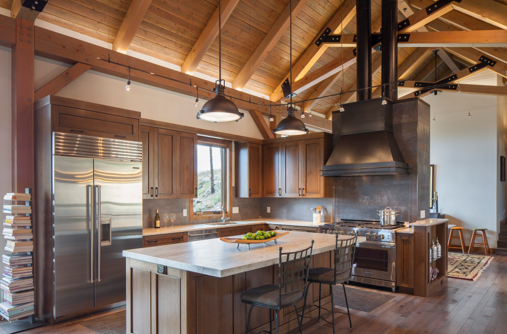 Country l-shaped kitchen in Denver with an undermount sink, recessed-panel cabinets, medium wood cabinets, brown splashback, stainless steel appliances, dark hardwood floors, with island, brown floor, white benchtop, exposed beam, vaulted and wood.