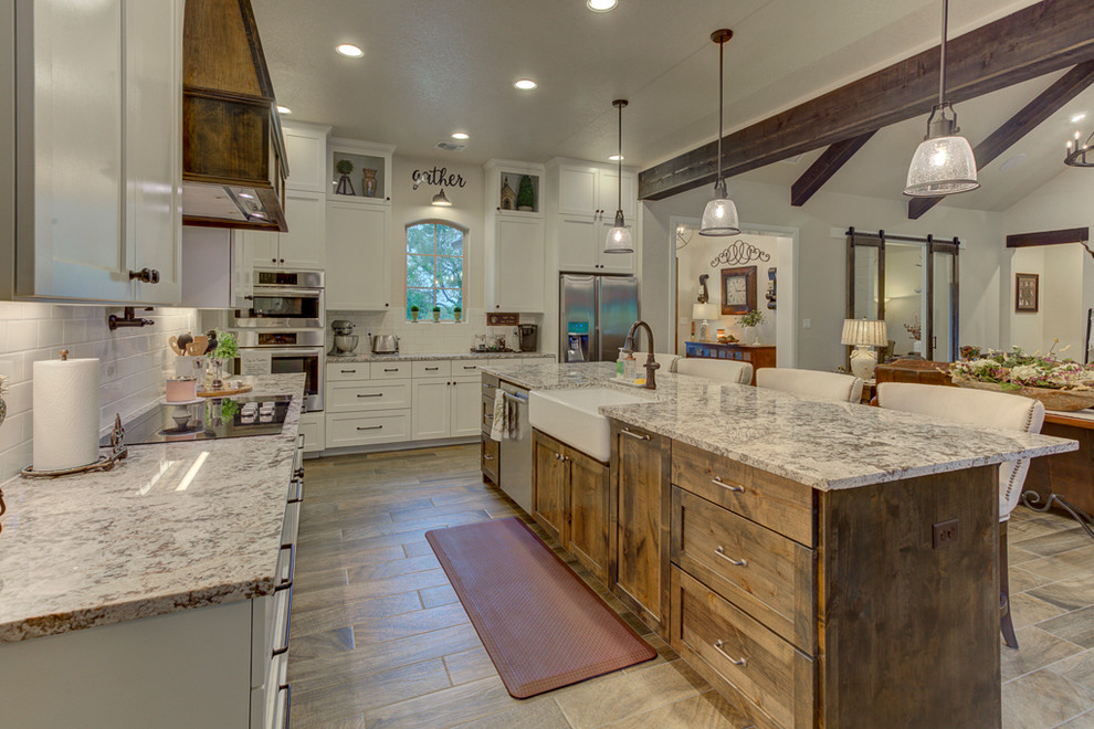 Photo of a mid-sized country galley eat-in kitchen in Austin with a farmhouse sink, shaker cabinets, white cabinets, granite benchtops, white splashback, subway tile splashback, stainless steel appliances, porcelain floors, with island, brown floor and beige benchtop.