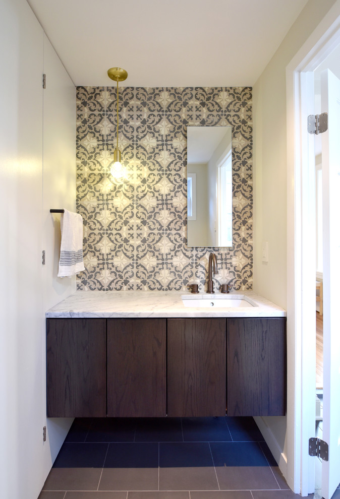 This is an example of a small powder room with flat-panel cabinets, brown cabinets, a one-piece toilet, cement tile, white walls, porcelain floors, an undermount sink, marble benchtops and grey floor.