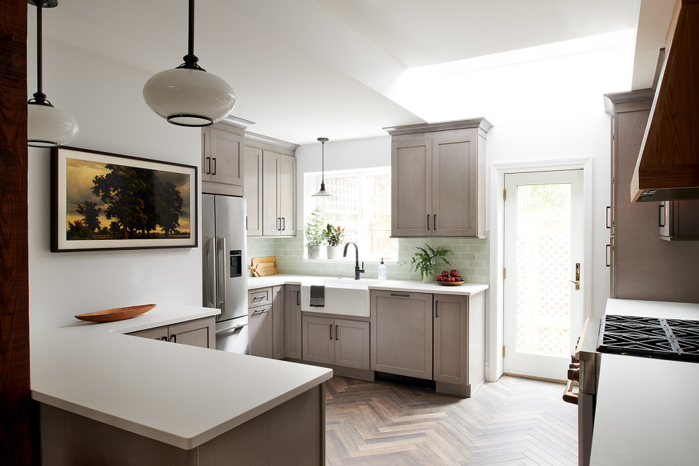 Mid-sized eclectic u-shaped eat-in kitchen in Philadelphia with a farmhouse sink, shaker cabinets, medium wood cabinets, quartzite benchtops, green splashback, glass tile splashback, white appliances, medium hardwood floors, with island, brown floor and white benchtop.