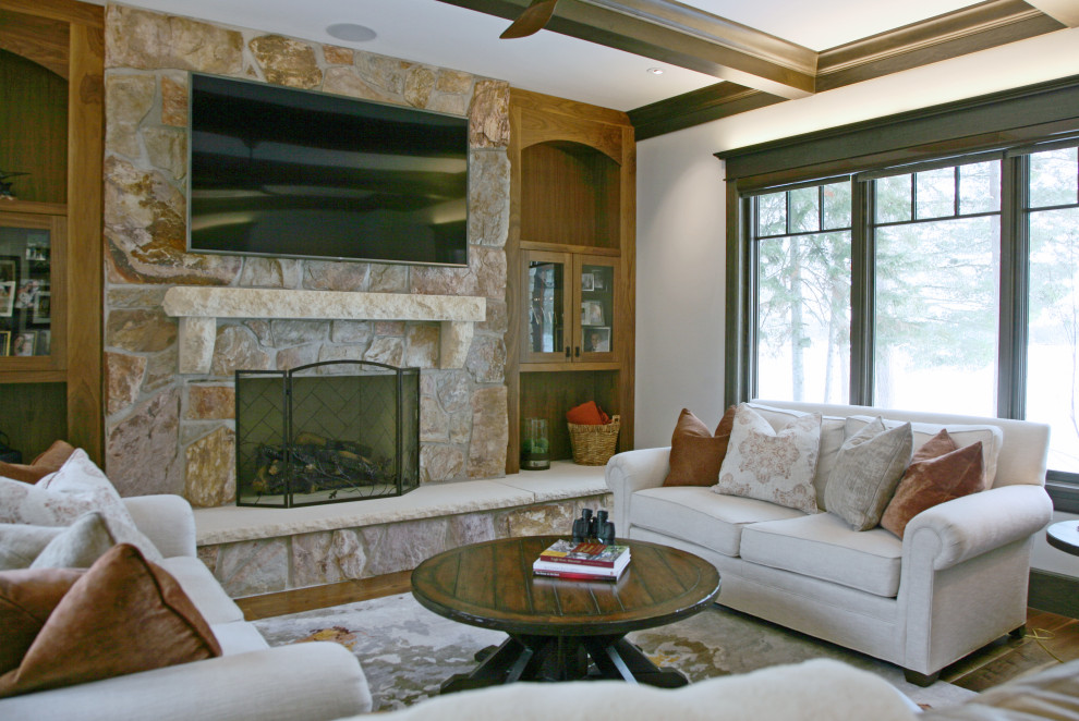 Cette image montre une salle de séjour traditionnelle de taille moyenne avec un mur beige, un sol en bois brun, une cheminée standard, un manteau de cheminée en pierre, un téléviseur fixé au mur et un plafond à caissons.