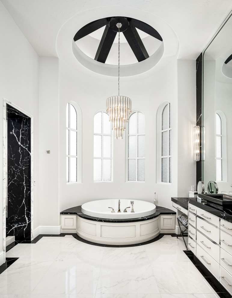 Свежая идея для дизайна: огромная главная ванная комната в стиле модернизм с белыми фасадами, накладной ванной, душевой комнатой, унитазом-моноблоком, белой плиткой, мраморной плиткой, белыми стенами, мраморным полом, накладной раковиной, мраморной столешницей, белым полом, открытым душем, черной столешницей, сиденьем для душа, тумбой под одну раковину, встроенной тумбой, кессонным потолком и панелями на части стены - отличное фото интерьера