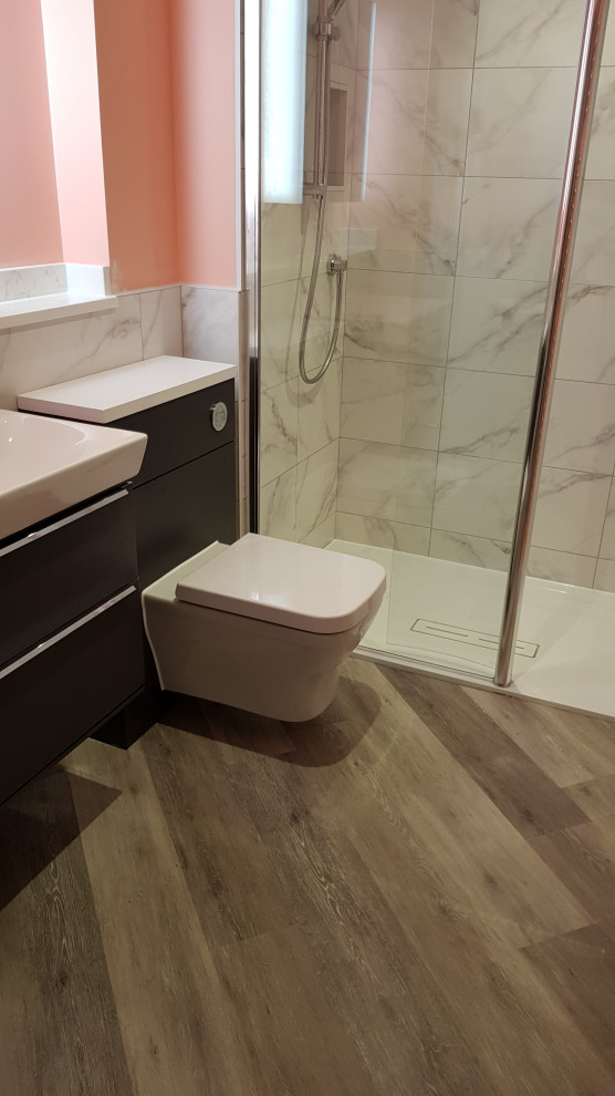 This is an example of a medium sized contemporary family bathroom in Kent with flat-panel cabinets, dark wood cabinets, a walk-in shower, a wall mounted toilet, grey tiles, ceramic tiles, pink walls, vinyl flooring, an integrated sink, solid surface worktops, grey floors, an open shower, white worktops, a single sink and a floating vanity unit.