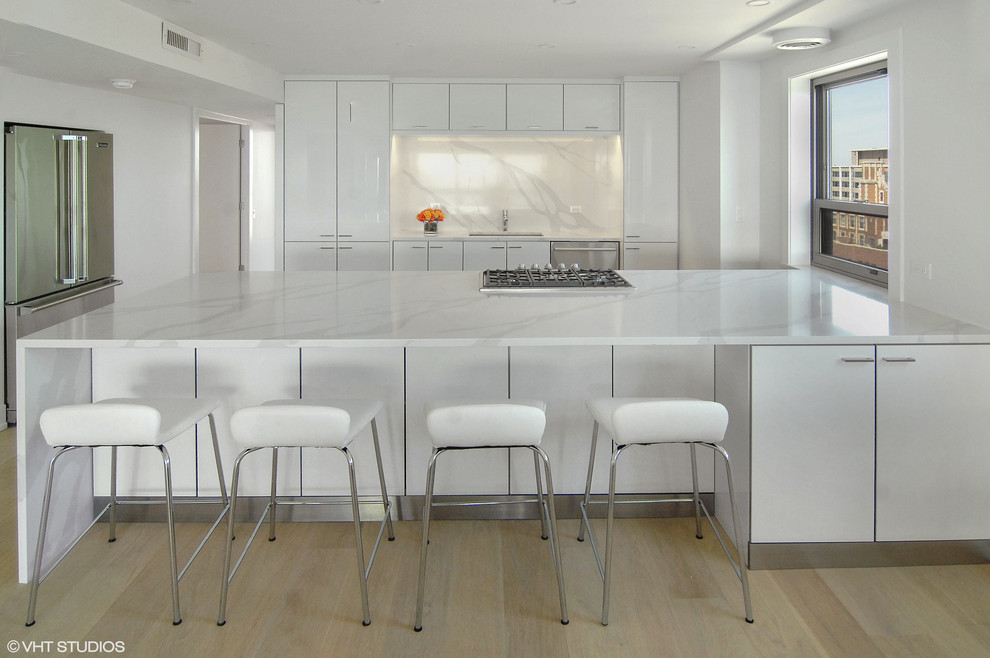 This is an example of a mid-sized modern galley kitchen in Chicago with a single-bowl sink, flat-panel cabinets, white cabinets, marble benchtops, white splashback, marble splashback, stainless steel appliances, light hardwood floors, beige floor and white benchtop.