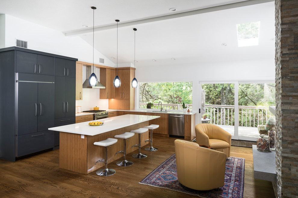 This is an example of a mid-sized contemporary l-shaped open plan kitchen in Austin with an undermount sink, flat-panel cabinets, quartzite benchtops, white splashback, panelled appliances, medium hardwood floors, with island and light wood cabinets.