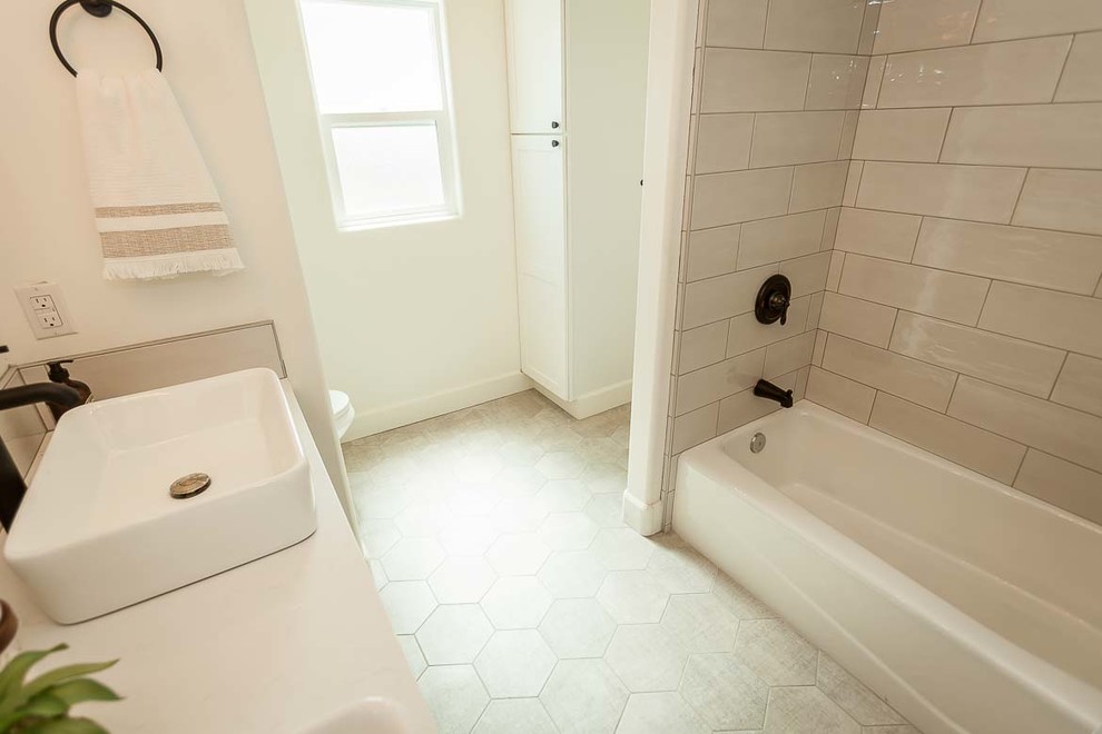 Inspiration for a mid-sized country master bathroom in San Luis Obispo with recessed-panel cabinets, dark wood cabinets, a drop-in tub, a shower/bathtub combo, a two-piece toilet, porcelain tile, white walls, ceramic floors, a vessel sink, engineered quartz benchtops, grey floor, a hinged shower door and white benchtops.