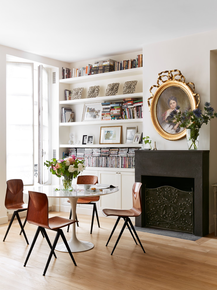 Photo of a scandinavian dining room in Paris with white walls, a standard fireplace, light hardwood floors and a plaster fireplace surround.