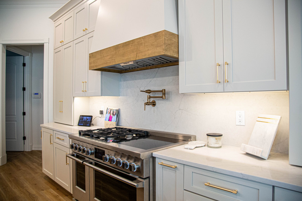 This is an example of a large transitional u-shaped eat-in kitchen in Indianapolis with an undermount sink, shaker cabinets, white cabinets, quartz benchtops, white splashback, engineered quartz splashback, stainless steel appliances, laminate floors, with island, blue floor, white benchtop and exposed beam.