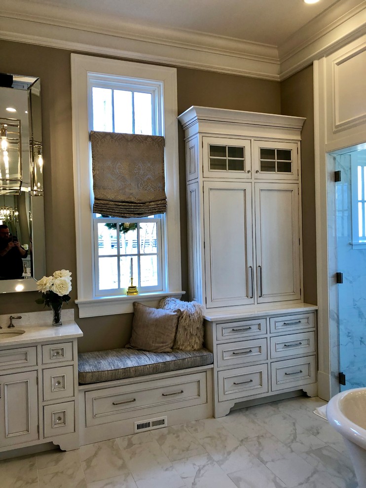 Photo of a country master wet room bathroom in DC Metro with beaded inset cabinets, white cabinets, a freestanding tub, white tile, porcelain tile, beige walls, porcelain floors, an undermount sink, marble benchtops, white floor, a hinged shower door and white benchtops.
