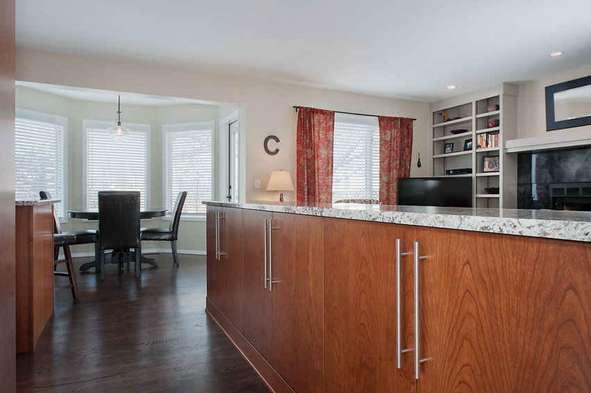 Mid-sized transitional u-shaped dark wood floor open concept kitchen photo in Calgary with an undermount sink, flat-panel cabinets, medium tone wood cabinets, granite countertops, white backsplash, mirror backsplash, stainless steel appliances and an island
