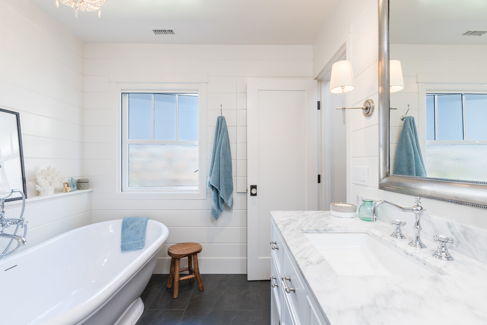 This is an example of a beach style 3/4 bathroom in San Luis Obispo with recessed-panel cabinets, white cabinets, a freestanding tub, a shower/bathtub combo, black walls, an undermount sink, marble benchtops, black floor and white benchtops.