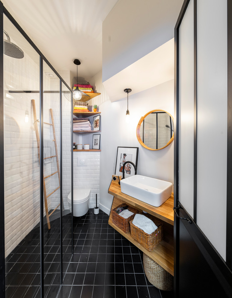 Small industrial 3/4 bathroom in Paris with a curbless shower, a wall-mount toilet, white tile, subway tile, white walls, cement tiles, a drop-in sink, wood benchtops, black floor, an open shower and beige benchtops.