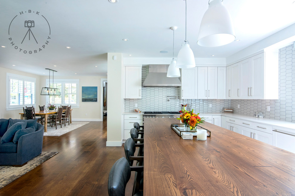 Example of a large single-wall medium tone wood floor and brown floor open concept kitchen design with an undermount sink, recessed-panel cabinets, white cabinets, wood countertops, white backsplash, ceramic backsplash, stainless steel appliances, an island and brown countertops