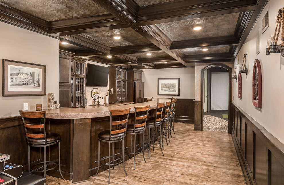 Photo of a traditional u-shaped home bar in Chicago with raised-panel cabinets, brown cabinets and brown floor.