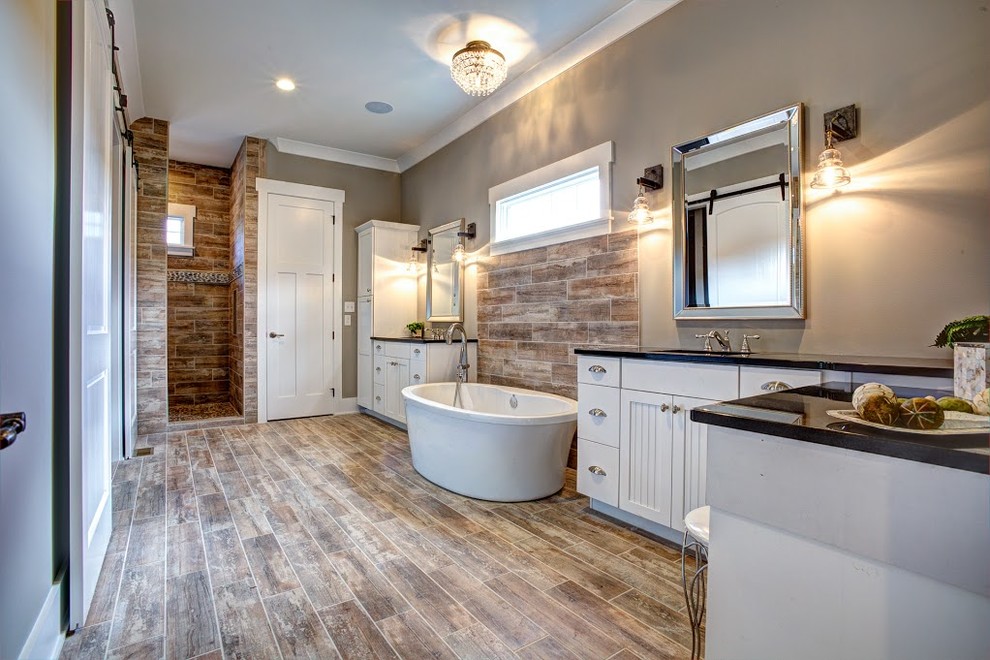 Photo of a large country master bathroom in Other with recessed-panel cabinets, white cabinets, a freestanding tub, an open shower, brown tile, porcelain tile, brown walls, dark hardwood floors, an undermount sink, brown floor and an open shower.