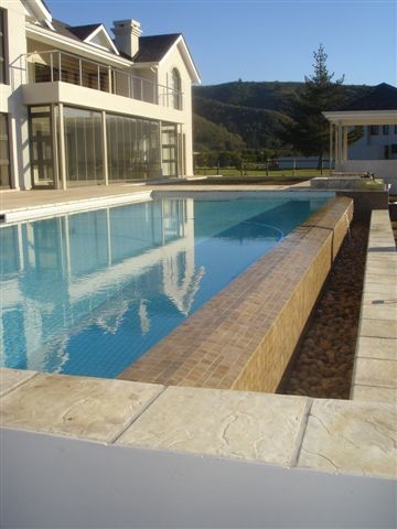This is an example of an expansive traditional backyard rectangular infinity pool in Other with natural stone pavers.
