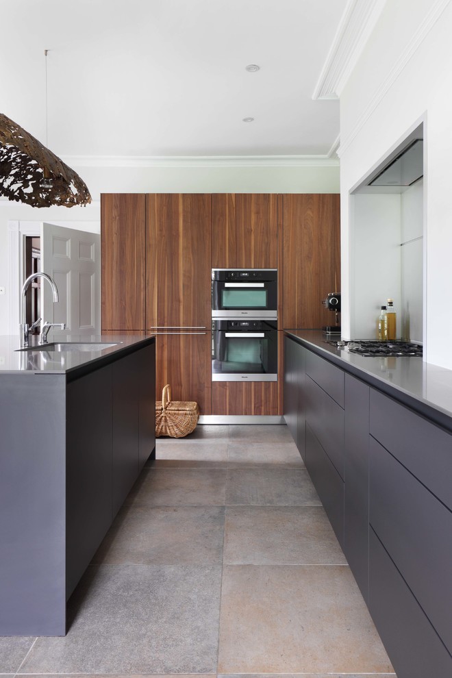 Photo of a large contemporary galley separate kitchen in London with black appliances, with island, an integrated sink, flat-panel cabinets and slate floors.