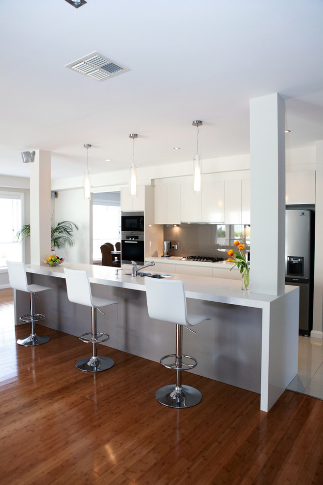 Design ideas for a large modern galley open plan kitchen in Sydney with an undermount sink, flat-panel cabinets, white cabinets, quartz benchtops, beige splashback, glass sheet splashback, stainless steel appliances, bamboo floors and with island.