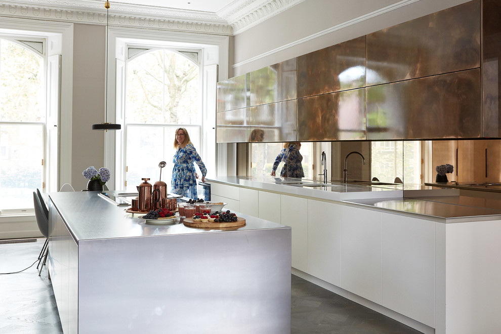 This is an example of a large contemporary single-wall open plan kitchen in London with flat-panel cabinets, white cabinets, stainless steel benchtops, metallic splashback, mirror splashback, with island, grey floor and grey benchtop.