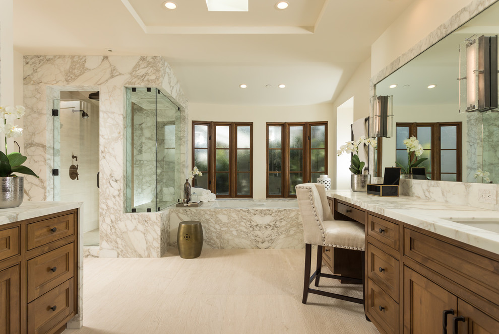 Design ideas for a mediterranean master bathroom in Orange County with recessed-panel cabinets, medium wood cabinets, an undermount tub, a corner shower, beige walls, an undermount sink, marble benchtops, beige floor and a hinged shower door.