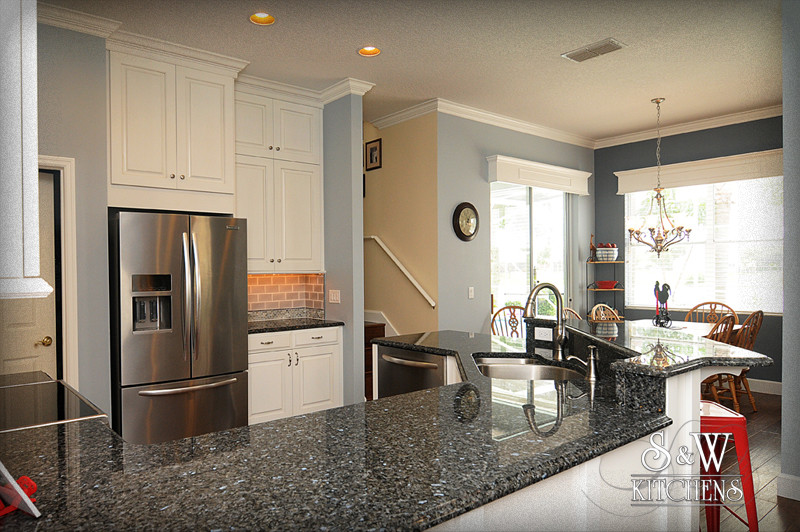 Open concept kitchen - mid-sized transitional u-shaped dark wood floor open concept kitchen idea in Orlando with a double-bowl sink, raised-panel cabinets, white cabinets, granite countertops, beige backsplash, subway tile backsplash and stainless steel appliances