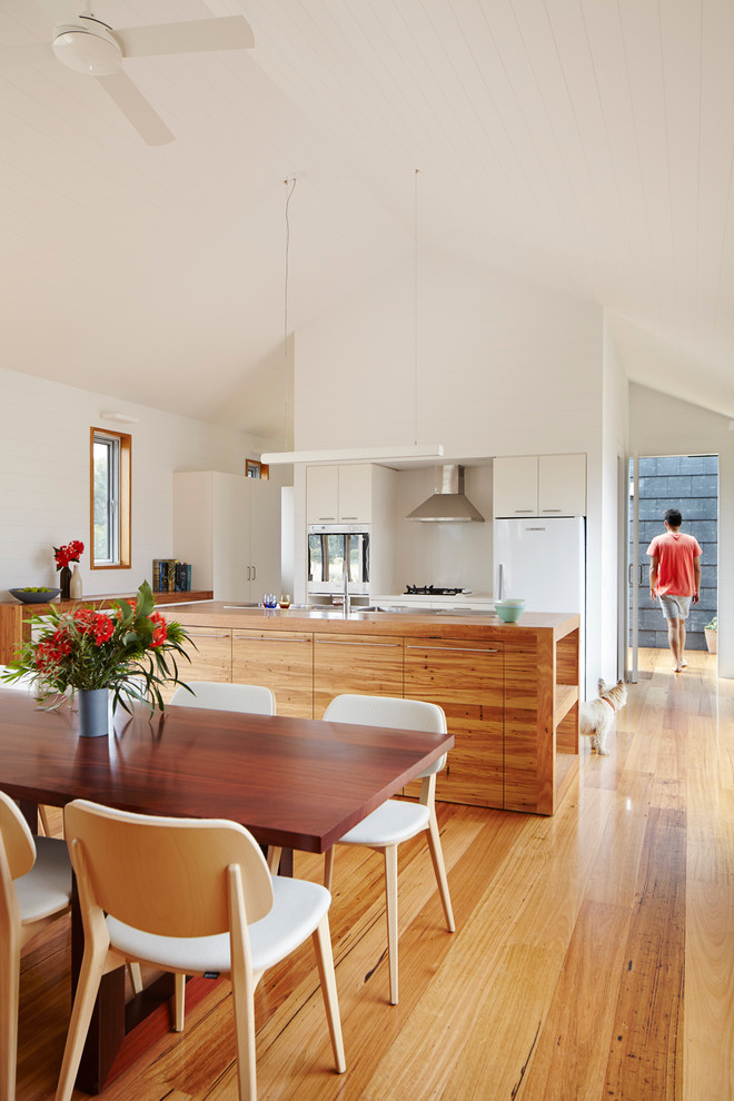 Photo of an eat-in kitchen in Geelong with a double-bowl sink, light wood cabinets, wood benchtops, stone slab splashback, white appliances, light hardwood floors and with island.