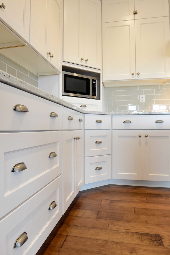 This is an example of a mid-sized arts and crafts l-shaped open plan kitchen in Other with an undermount sink, shaker cabinets, white cabinets, quartz benchtops, beige splashback, glass tile splashback, stainless steel appliances, medium hardwood floors and with island.