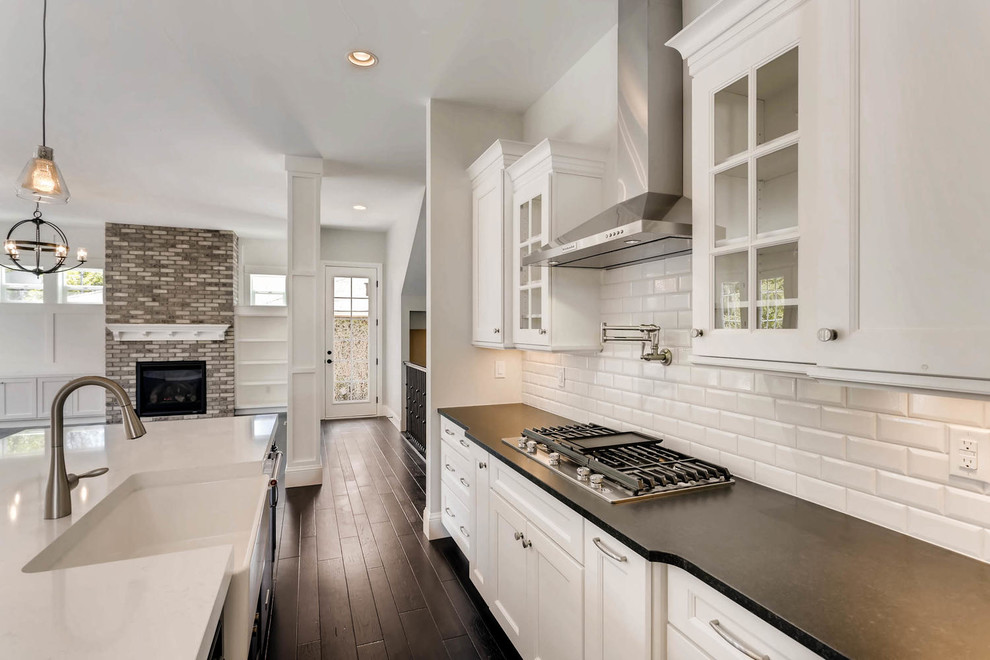 Open concept kitchen - large transitional l-shaped dark wood floor and brown floor open concept kitchen idea in Denver with recessed-panel cabinets, white cabinets, ceramic backsplash, stainless steel appliances and an island