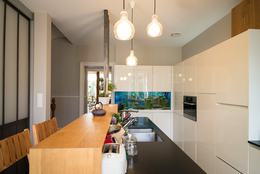Inspiration for a large transitional single-wall eat-in kitchen in Nantes with an undermount sink, flat-panel cabinets, white cabinets, granite benchtops, multi-coloured splashback, cement tile splashback, stainless steel appliances, ceramic floors and with island.