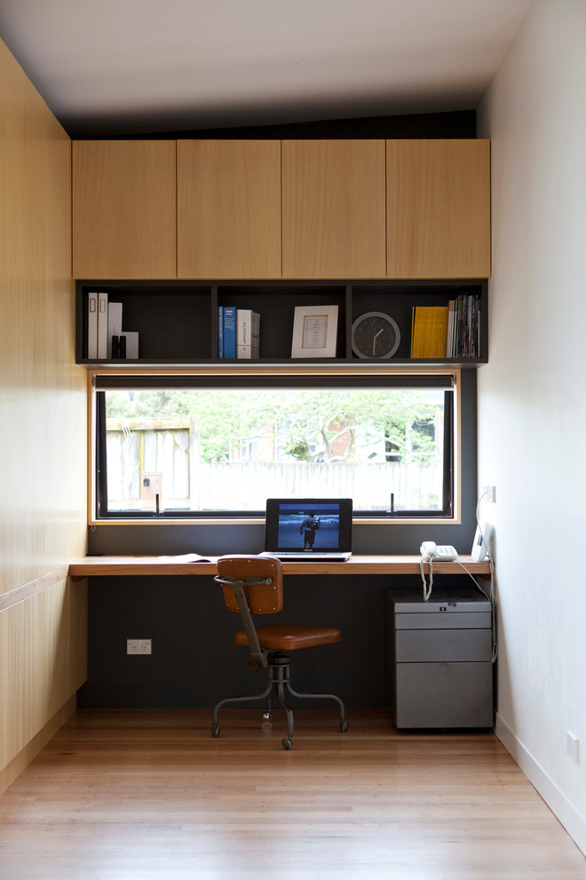 This is an example of a small contemporary home office in Auckland with white walls, medium hardwood floors and a built-in desk.