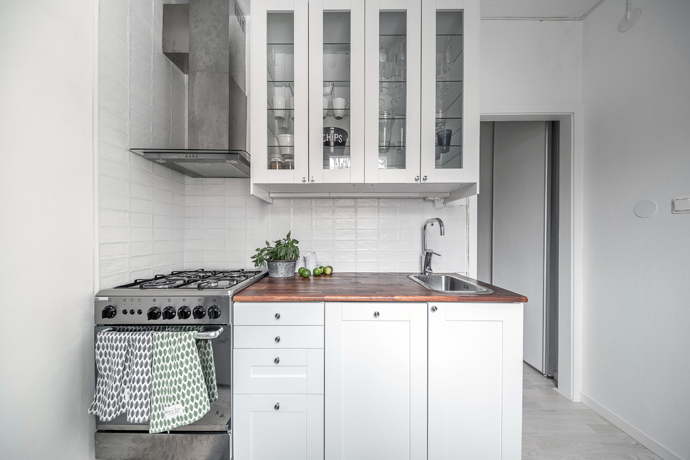 Design ideas for a small scandinavian separate kitchen in Stockholm with a single-bowl sink, glass-front cabinets, white cabinets, wood benchtops, stainless steel appliances and no island.
