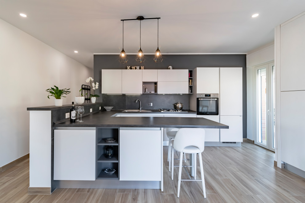 Large contemporary u-shaped eat-in kitchen in Rome with an undermount sink, flat-panel cabinets, white cabinets, wood benchtops, black splashback, porcelain splashback, stainless steel appliances, porcelain floors, a peninsula, black benchtop and recessed.