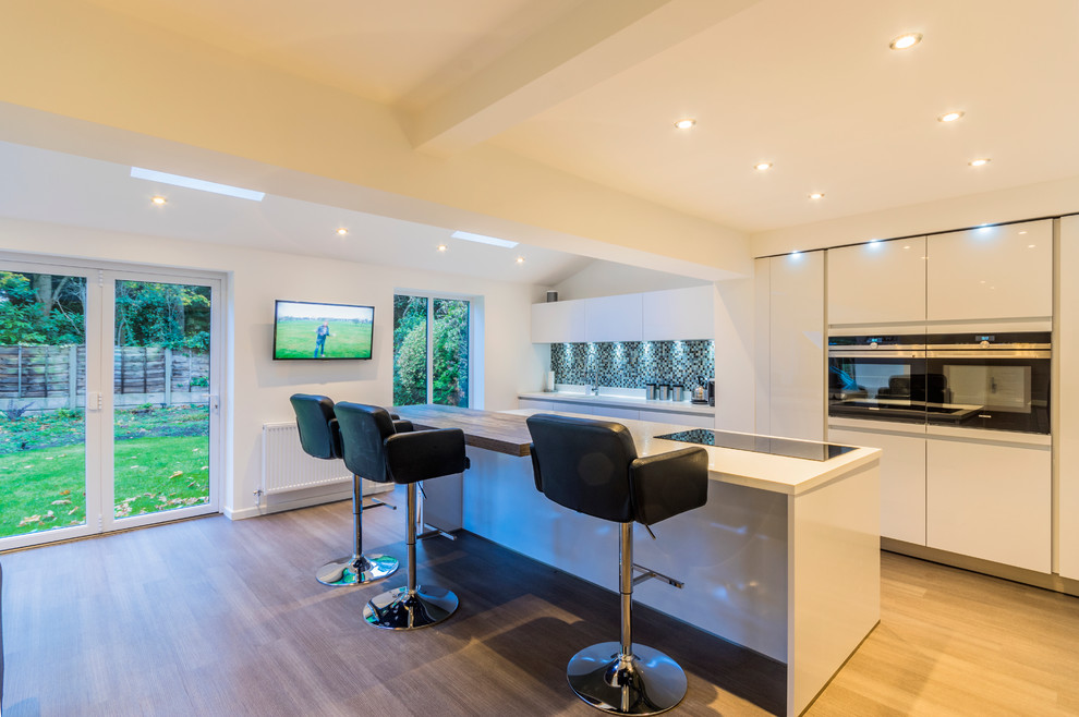 This is an example of a modern kitchen/diner in Cheshire with flat-panel cabinets, white cabinets, medium hardwood flooring and an island.