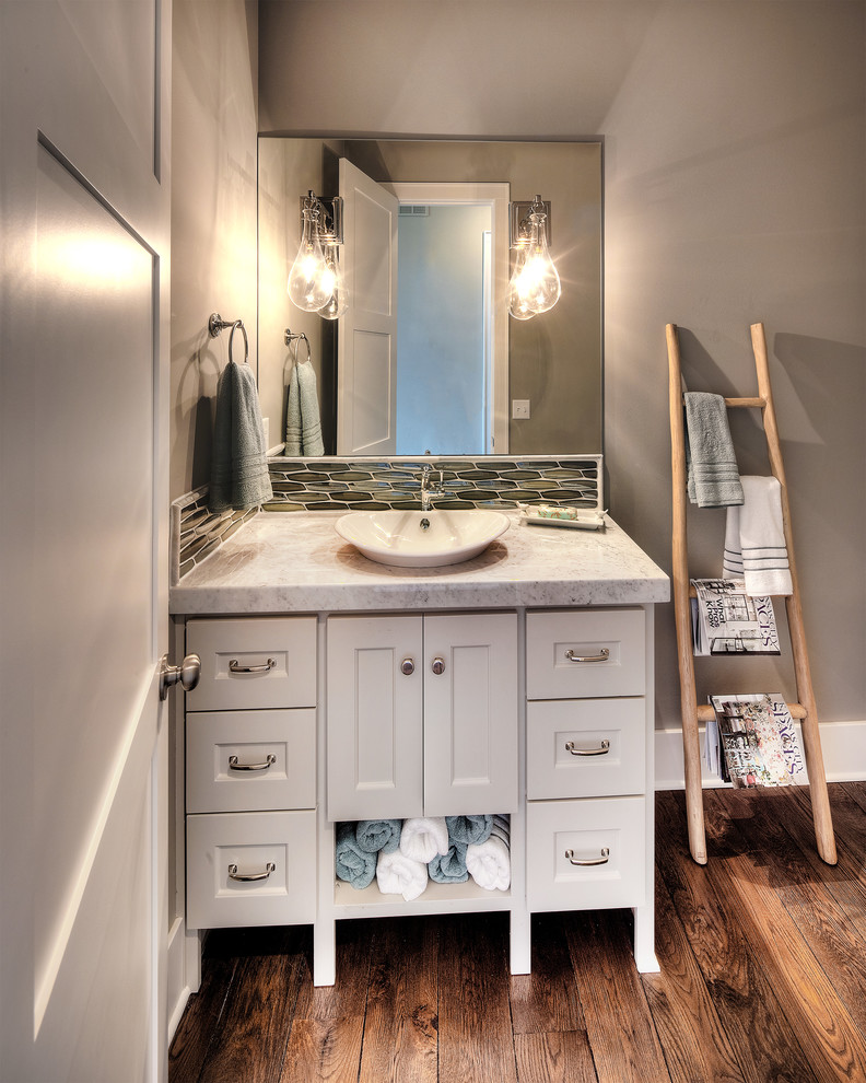 Design ideas for a transitional powder room in Kansas City with recessed-panel cabinets, white cabinets, green tile, grey walls, dark hardwood floors, a vessel sink, brown floor and grey benchtops.